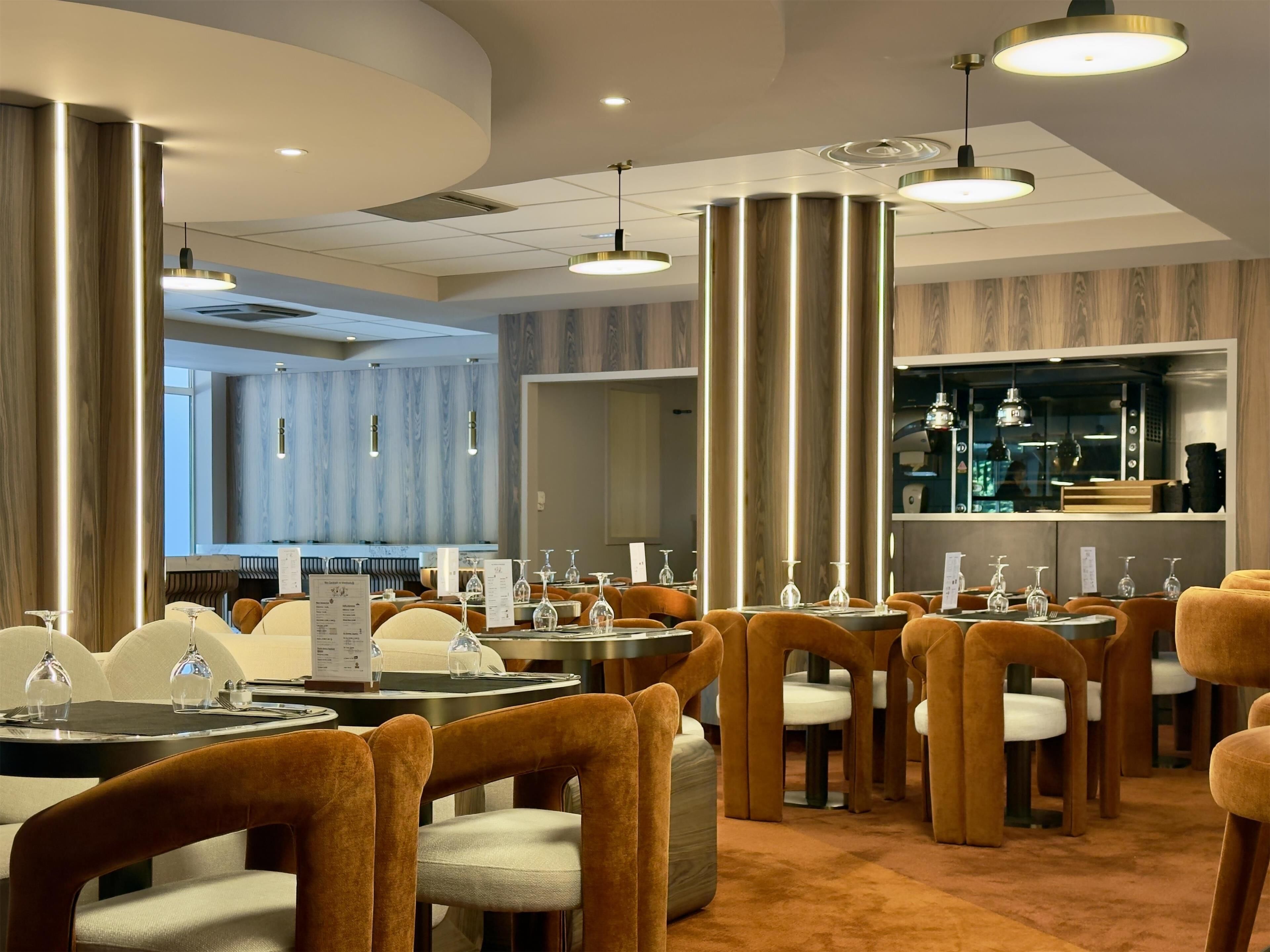 Un restaurante moderno con mesas redondas, sillas naranjas e iluminación colgante.