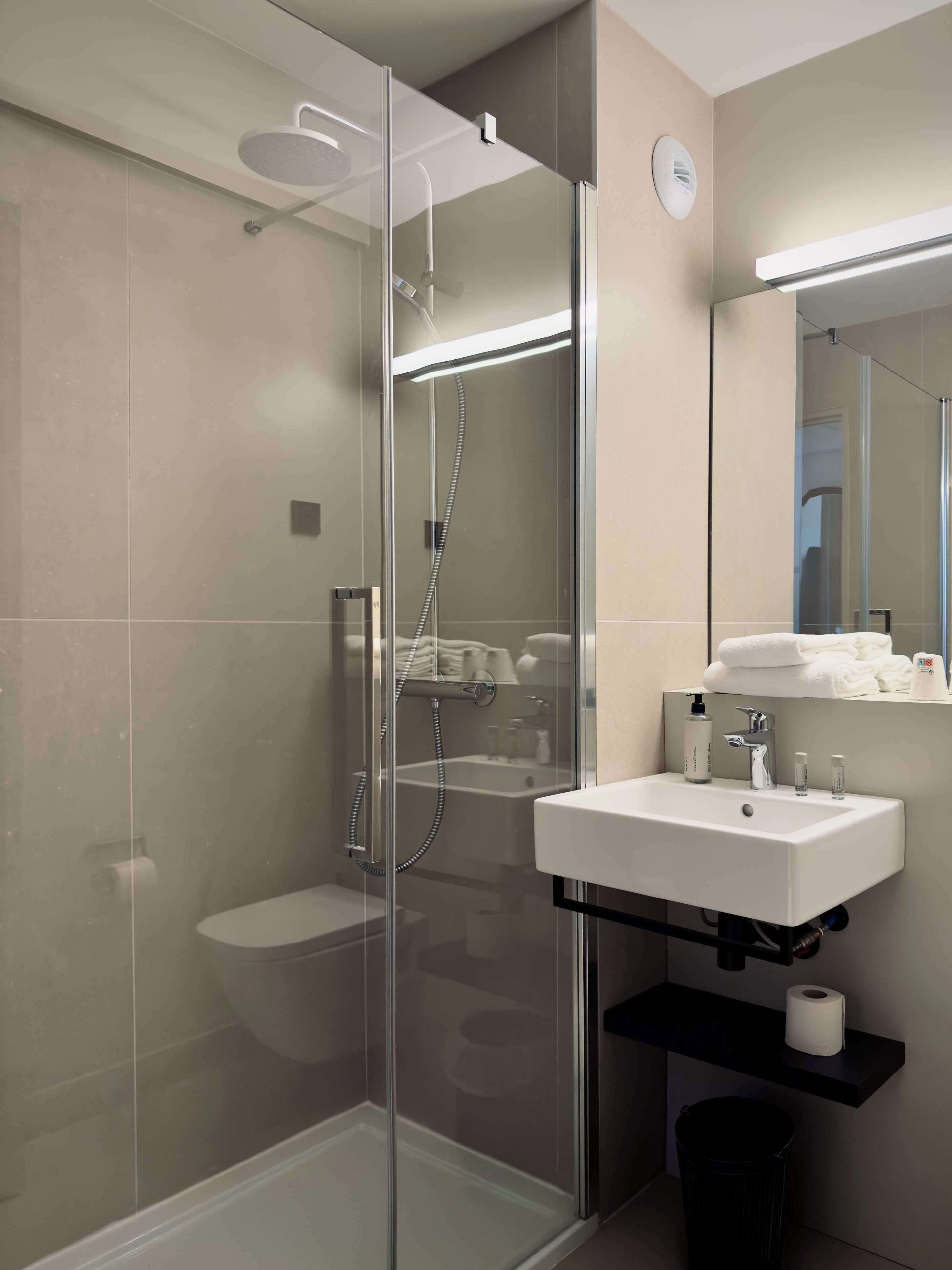 A modern bathroom with a glass-enclosed shower, a white sink, and a mirror above it.