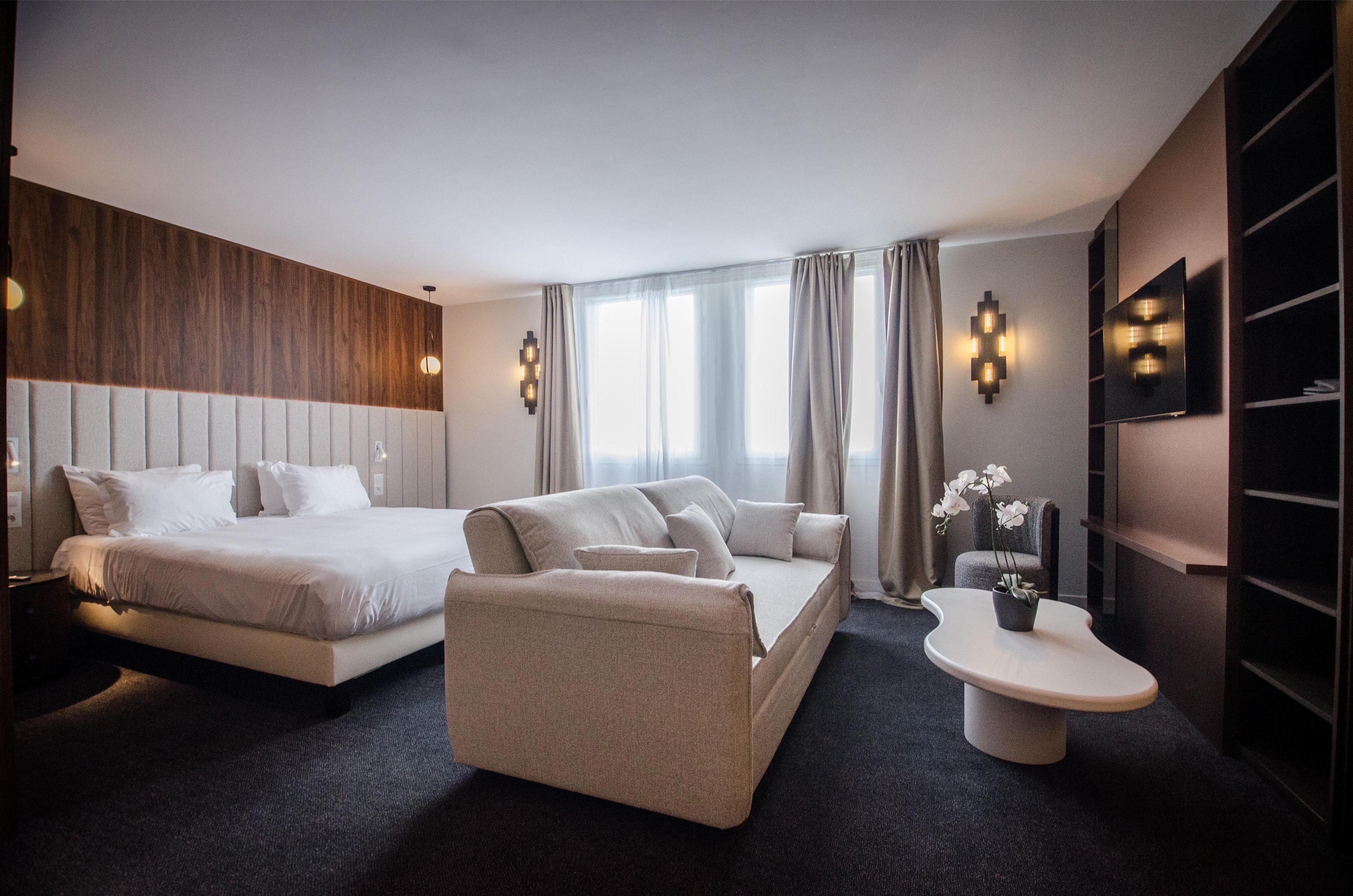 A modern hotel room with a bed, sofa, bedside table, and a TV.