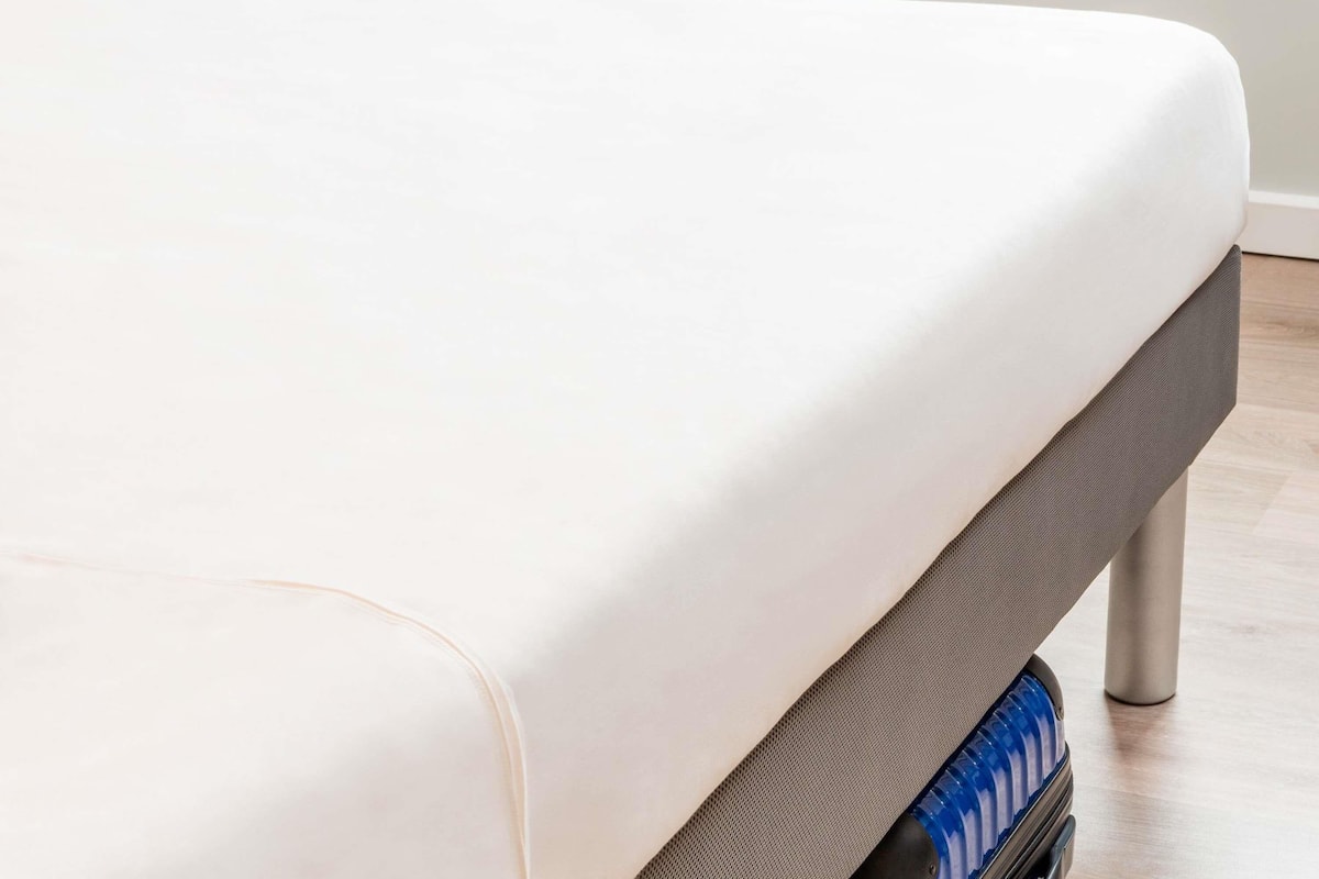 A bed with a white mattress and a grey headboard.