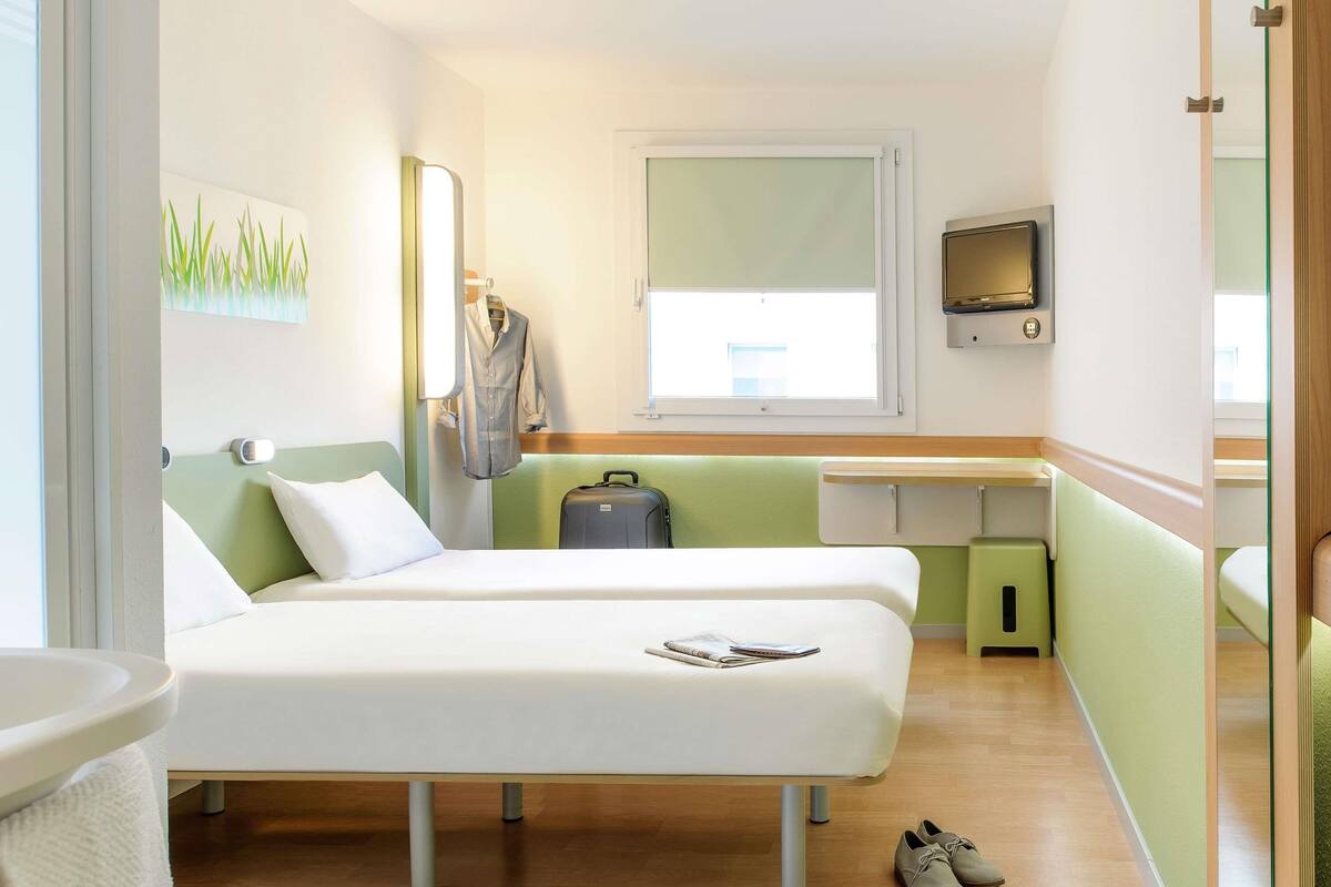Una habitación de hotel moderna con dos camas, un escritorio, un televisor y una maleta.