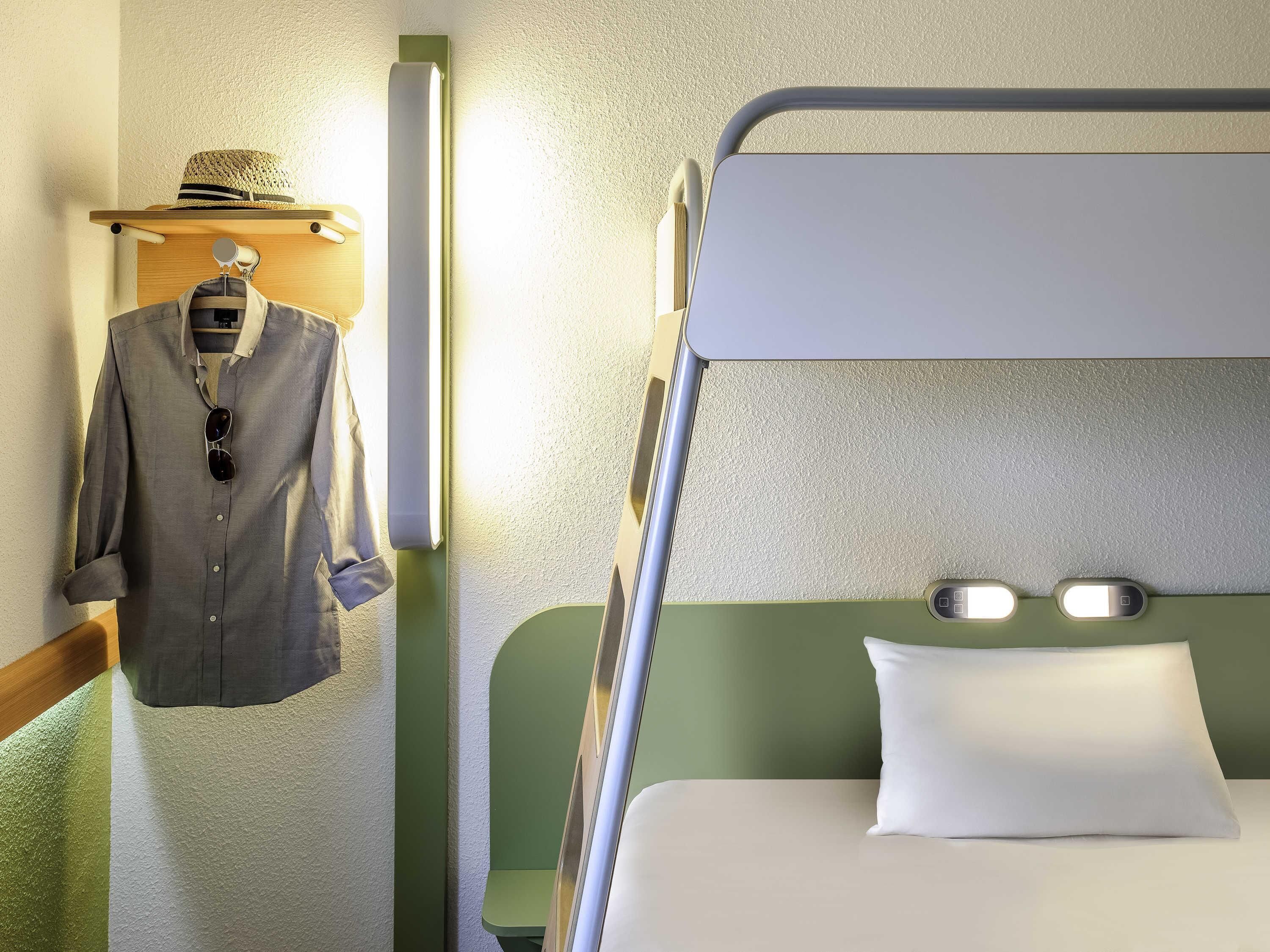 A bunk bed with a pillow, a hanging shirt, and a hat on a shelf.