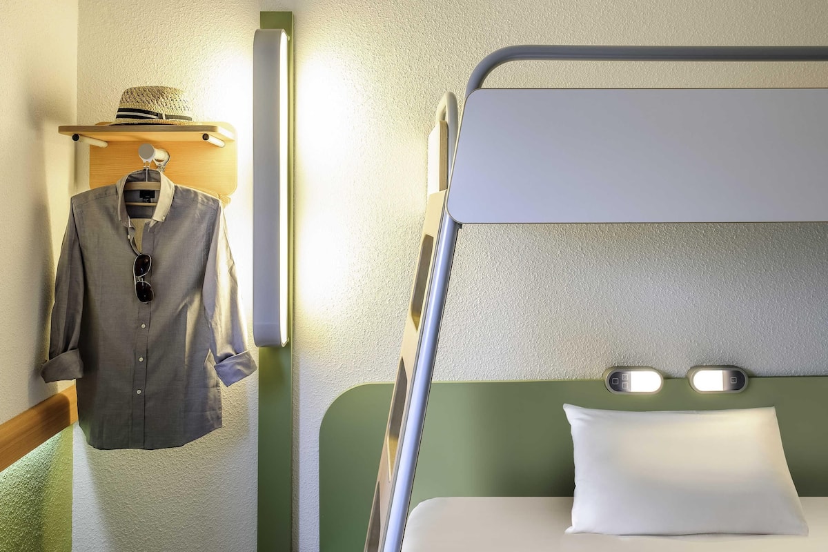A bunk bed with a pillow, a hanging shirt, and a hat on a shelf.