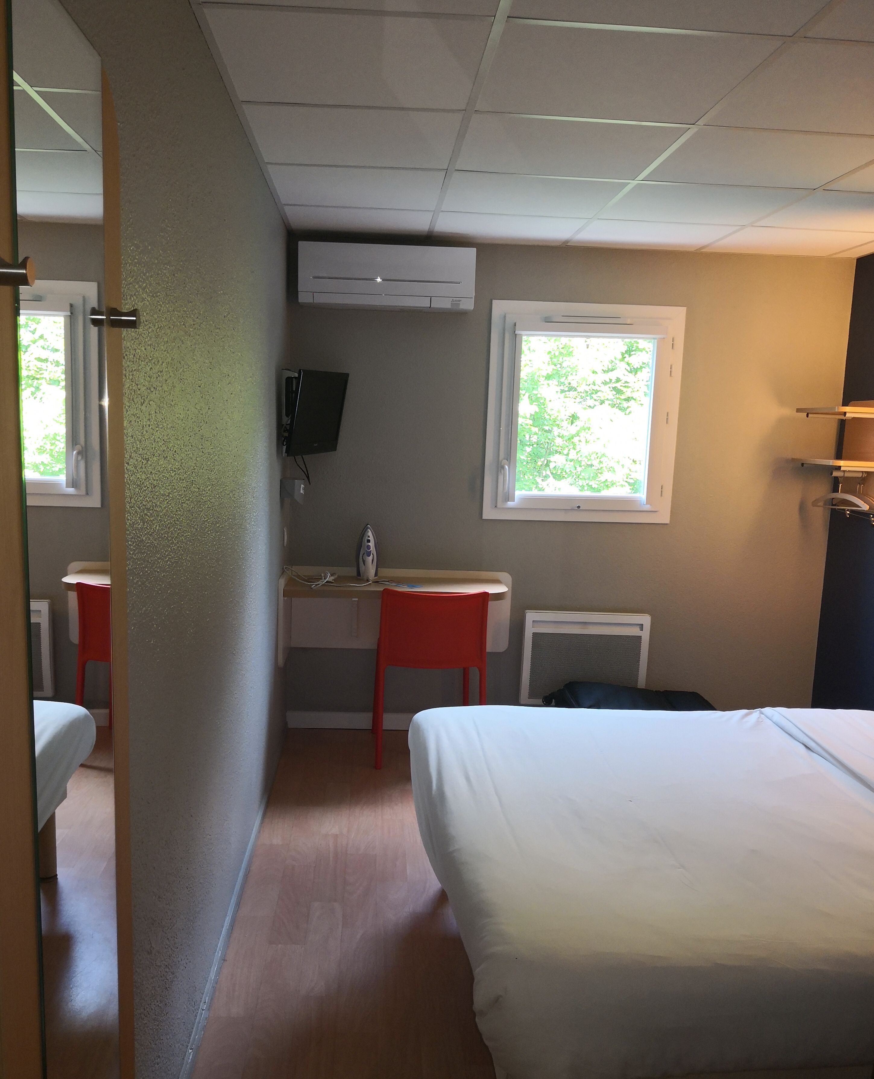 A hotel room with a bed, a desk, a chair, a television, and a window.