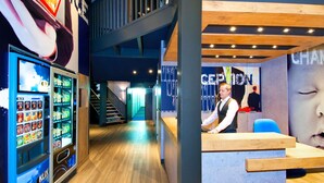 A modern interior with a reception desk, a staircase, and a vending machine. - ibis budget Cergy Saint Christophe (Osny)