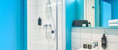 Un baño moderno con cabina de ducha de vidrio, un lavamanos blanco con un espejo encima y una pared de acento azul.