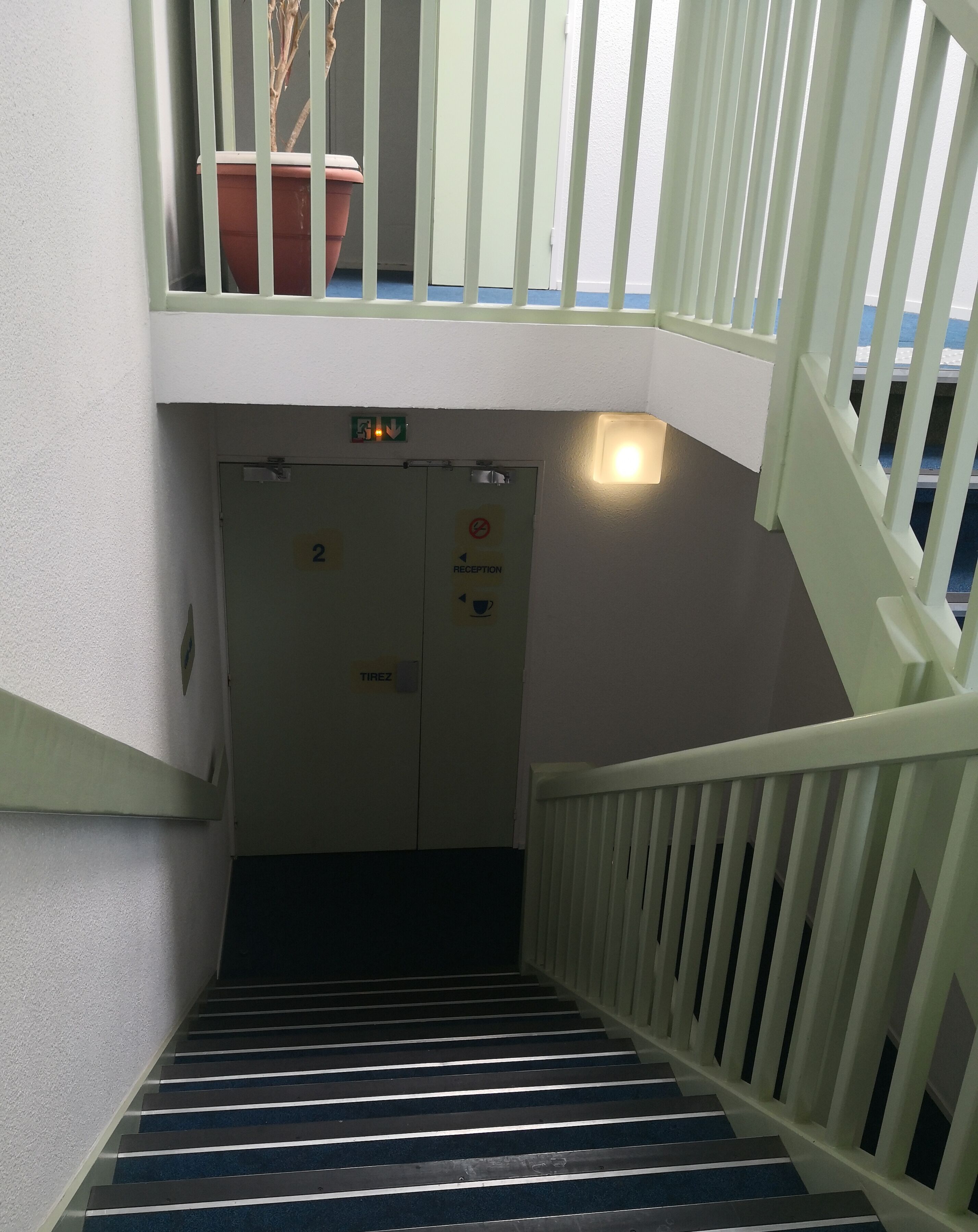 Eine Treppe mit weißen Geländern führt zu einem Empfangsbereich, der mit einem 'Reception'-Schild und einem 'Tirez'-Schild gekennzeichnet ist.