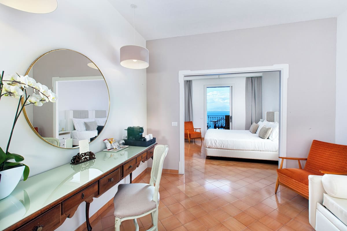 Una camera d'albergo con un letto, una scrivania, una sedia, uno specchio grande e vista sull'oceano.