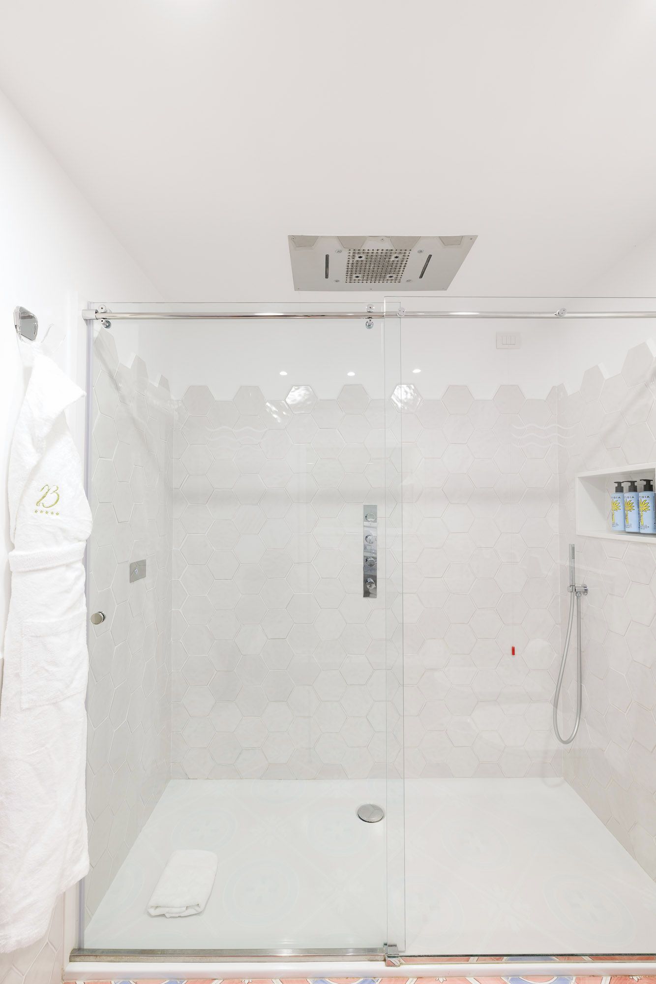 A glass-enclosed shower stall with a white tiled wall and a showerhead.