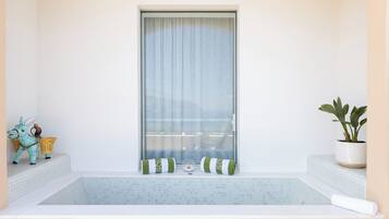 A bathroom with a bathtub, a window with curtains, a potted plant, and a decorative donkey figurine.