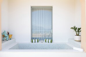 Un baño con bañera, una ventana con cortinas, una planta en maceta y una figurita decorativa de burro.