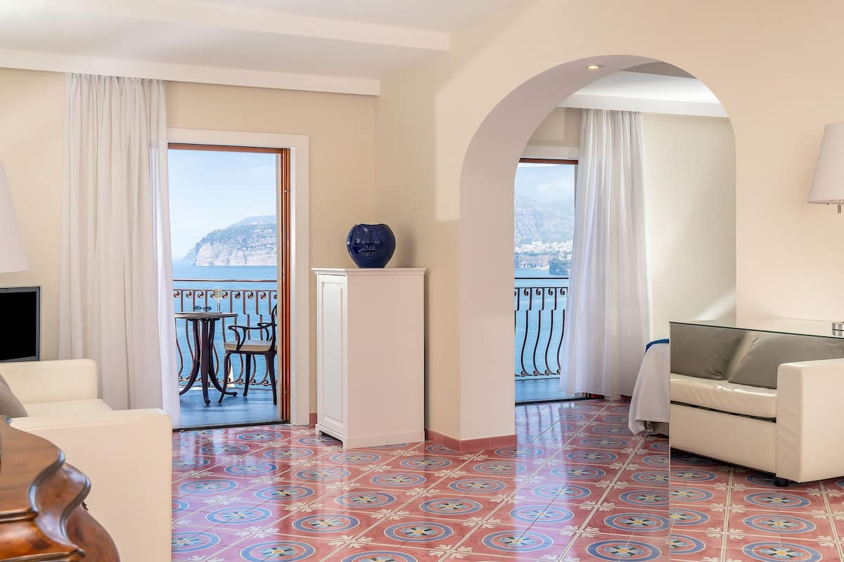 Camera d'albergo con balcone, divano, televisore e pavimento decorato.