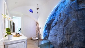 Une salle de bain moderne avec un meuble-lavabo blanc, un grand miroir et un mur en pierre illuminé de lumière bleue.