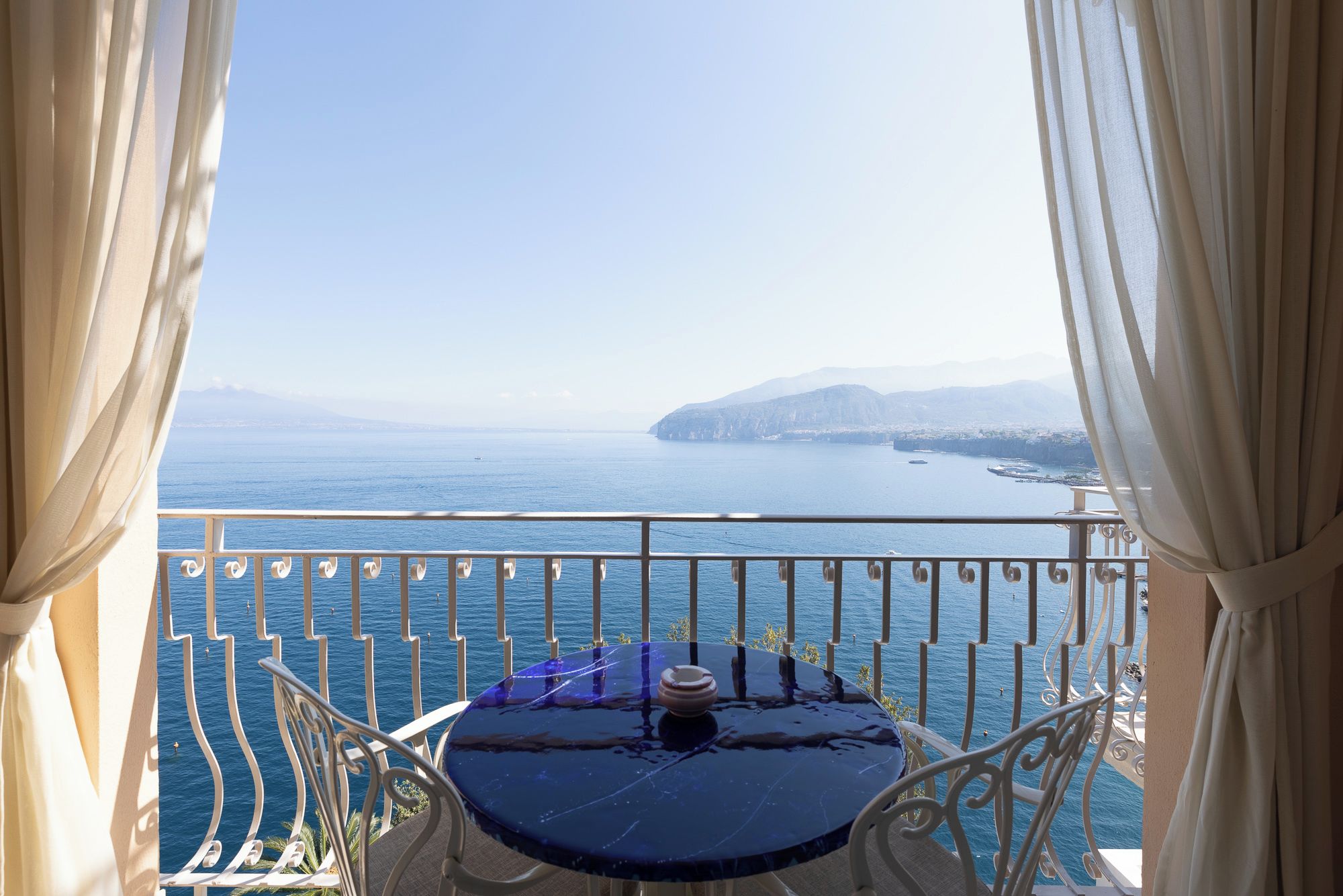 Un balcon avec une table et des chaises, offrant une vue sur la côte et les montagnes au loin.