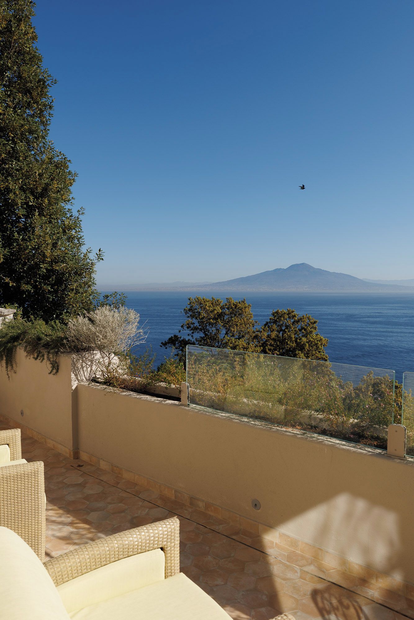 A terrace with wicker furniture, a view of the sea, and a mountain in the distance.