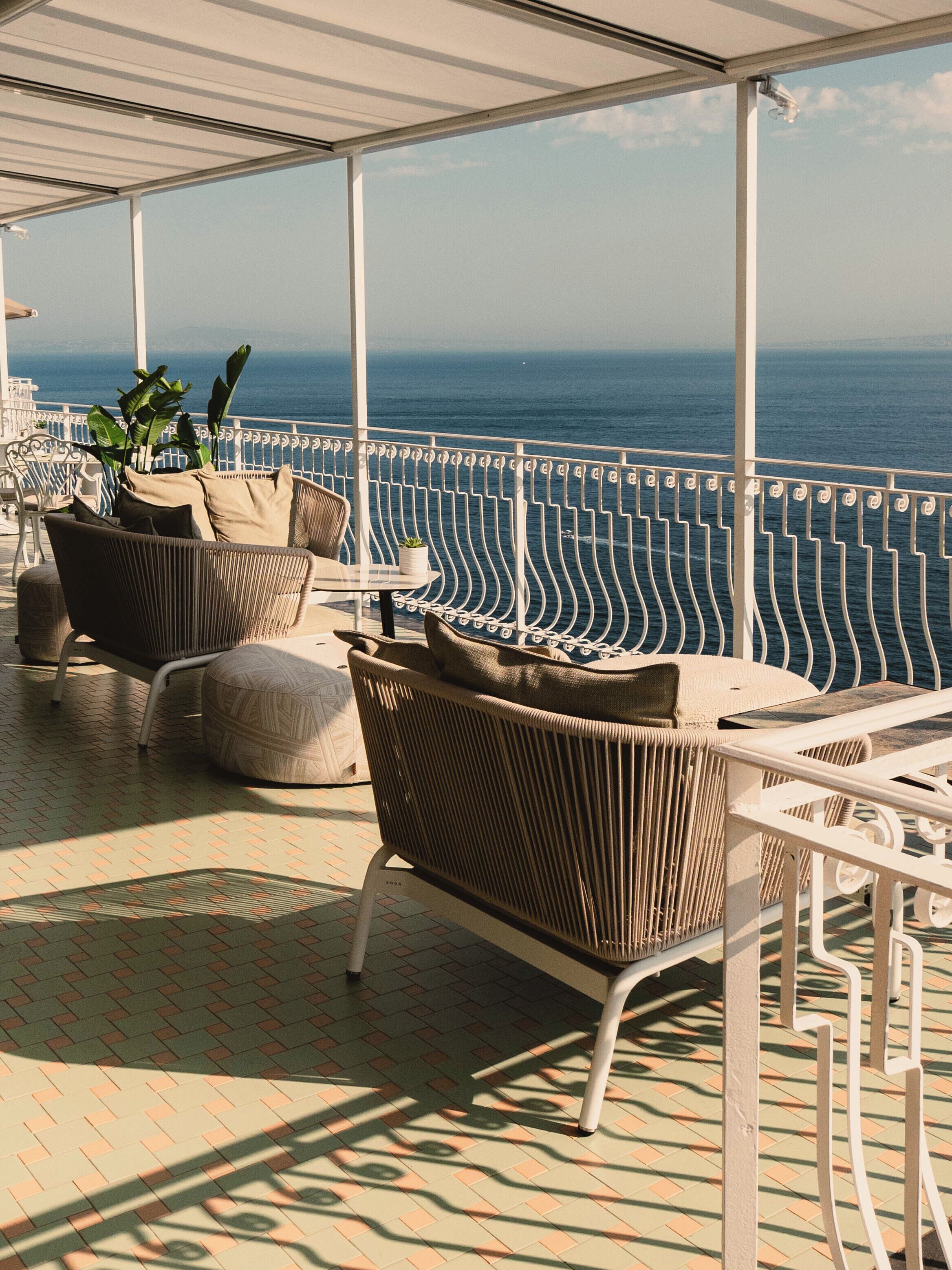 A covered outdoor seating area with wicker furniture and a view of the sea.