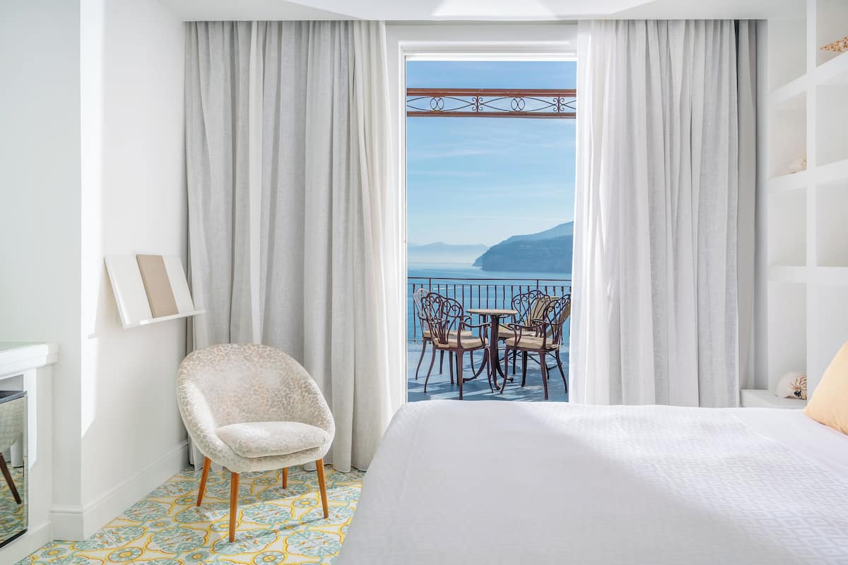 Una camera d'albergo con un letto, una sedia, un tavolo e vista sul mare.