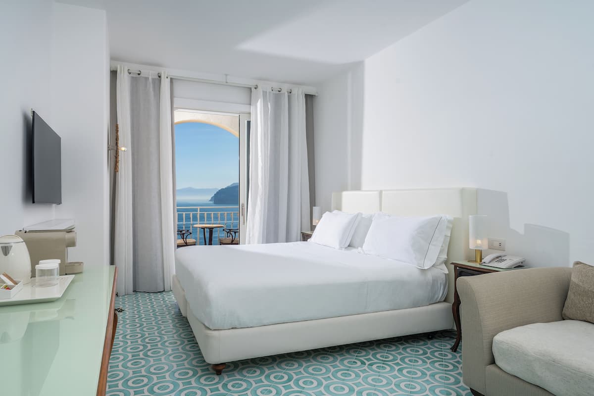 Una camera d'hotel con un letto, una scrivania, una sedia, una televisione e vista sul mare.
