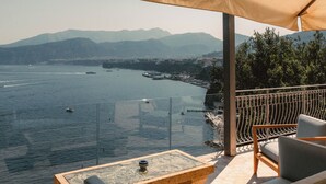 Una terrazza con tavolo e sedie, affacciata su uno specchio d'acqua con barche e montagne in lontananza.