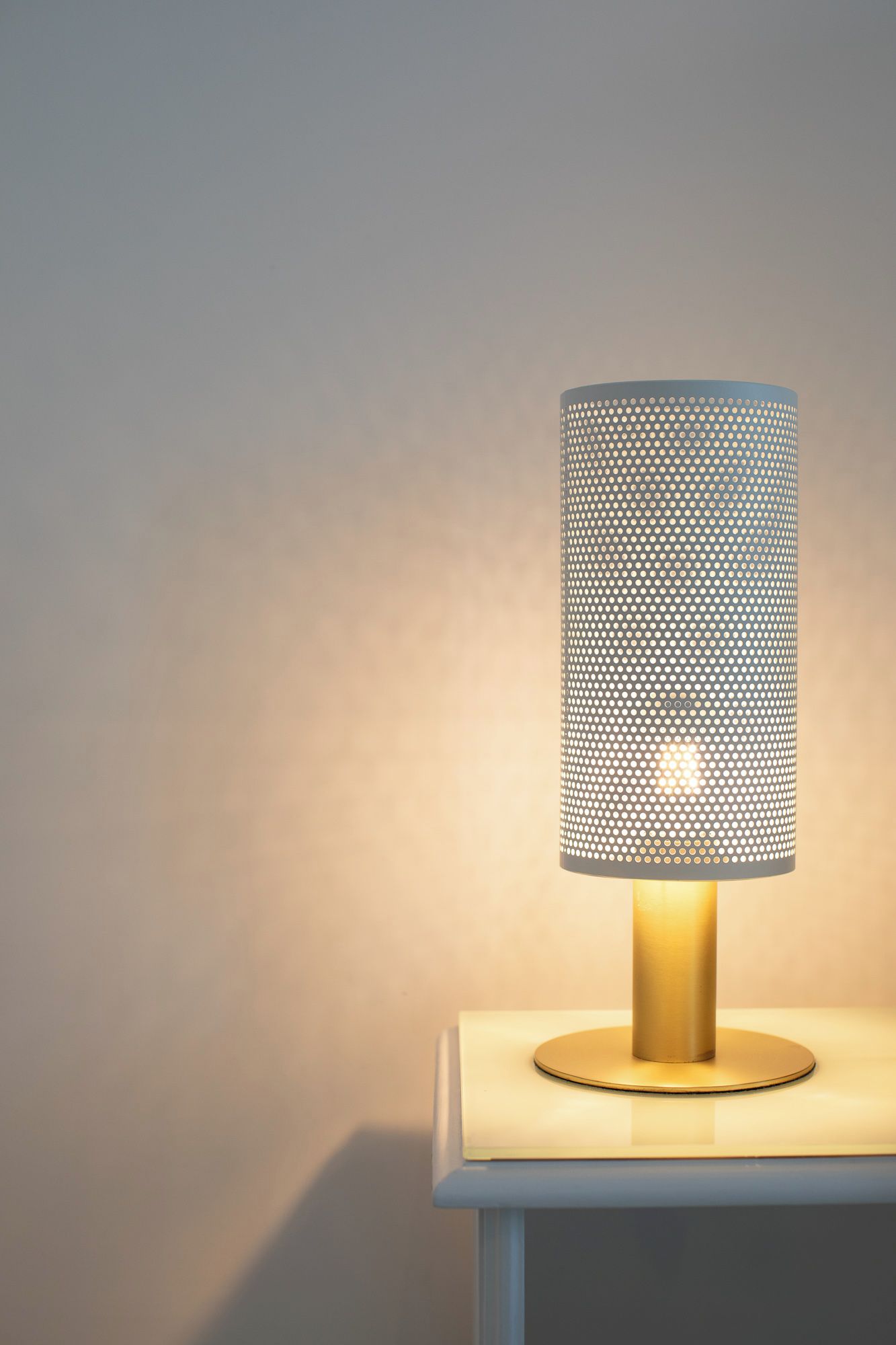 A table lamp with a perforated shade on a white table against a plain wall.