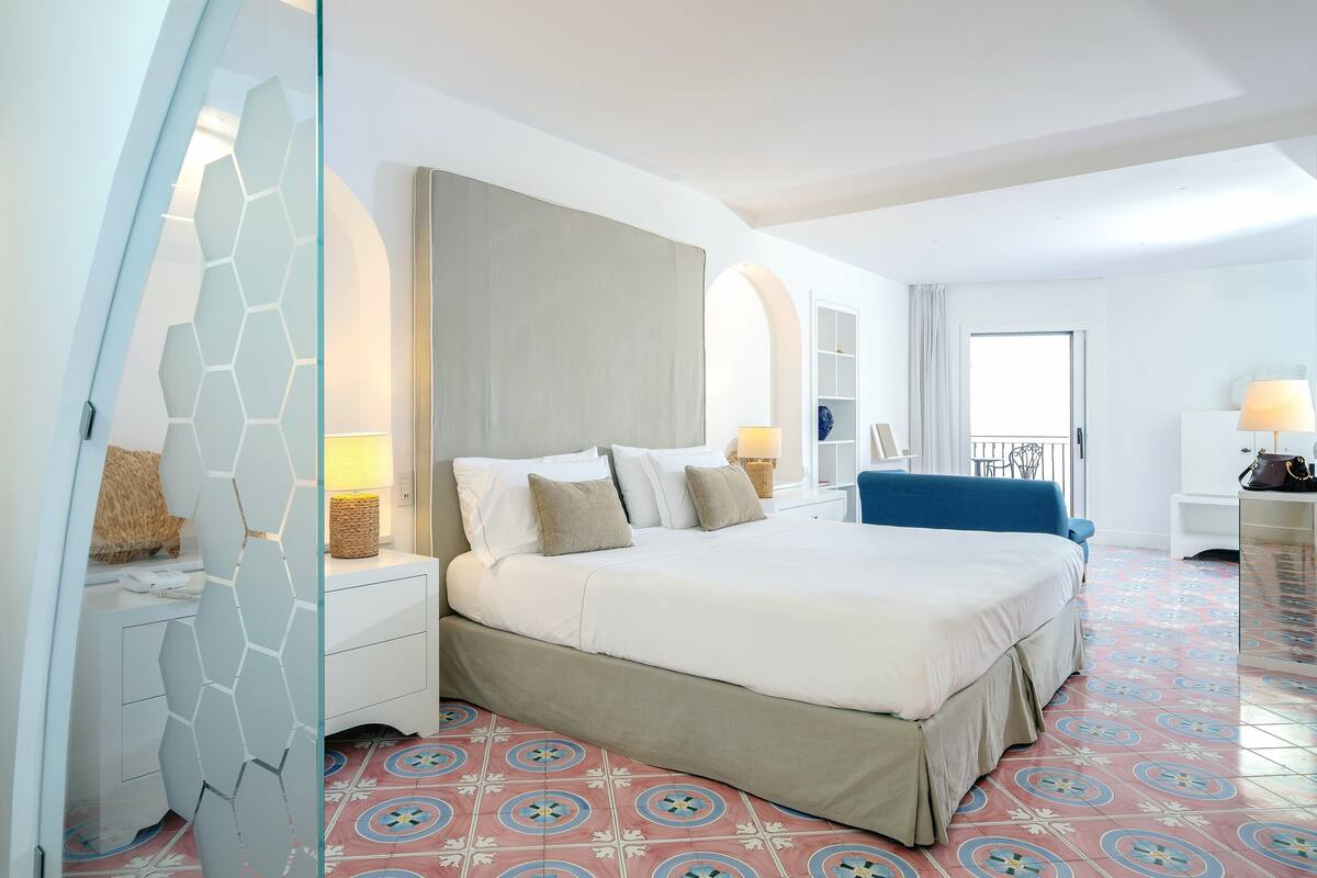 Una camera d'albergo con un letto grande, una scrivania con una lampada, una sedia e vista all'esterno.