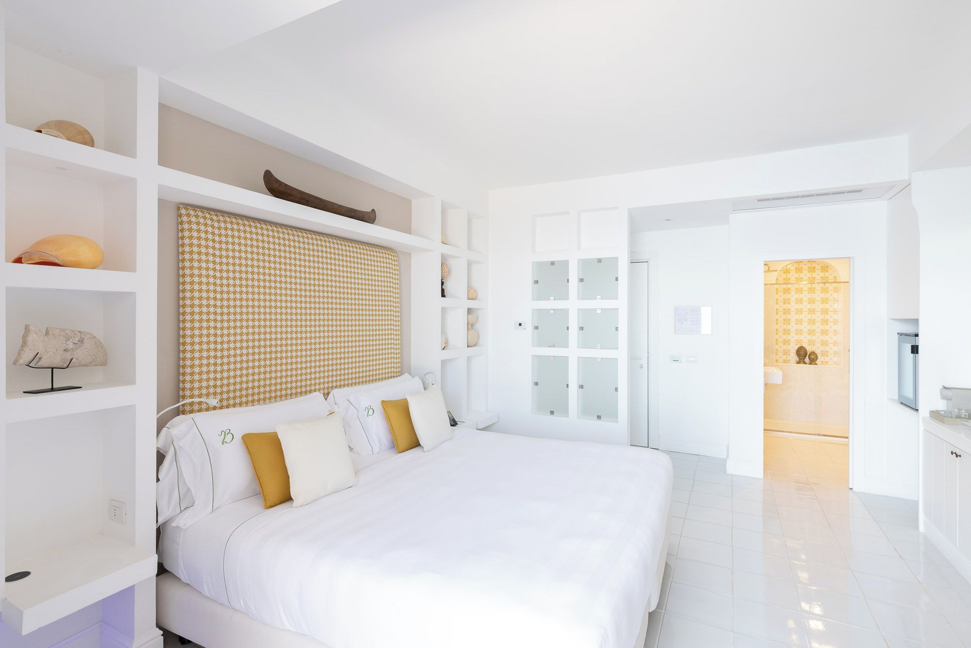 Een moderne slaapkamer met een groot bed, inbouwkasten en een badkamer met een glazen deur.