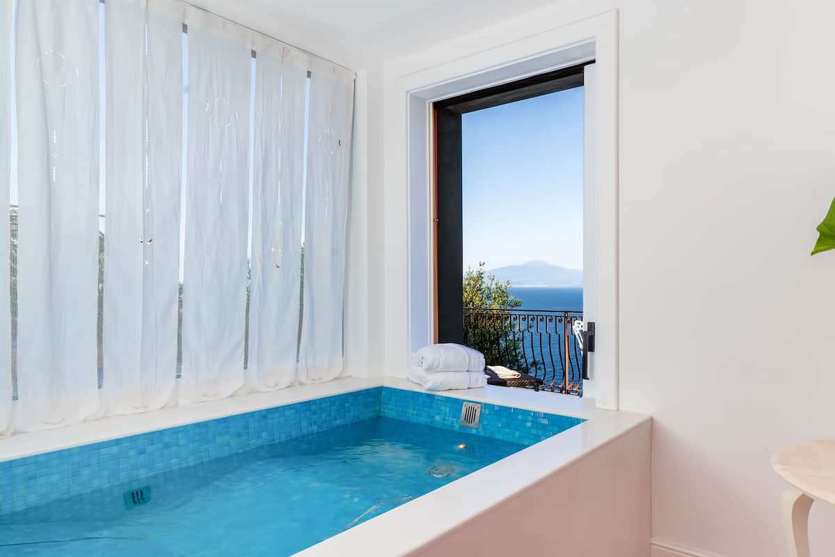Un piccolo balcone con vista sul mare, una vasca idromassaggio e una pianta in vaso.