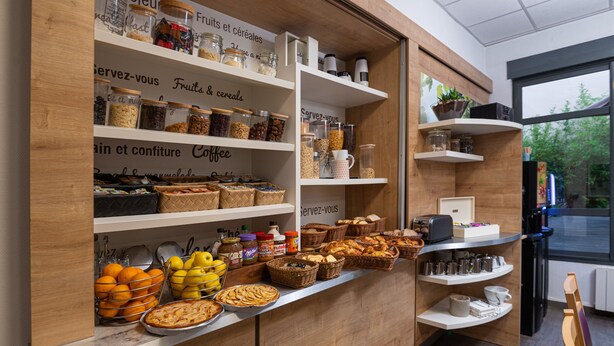 A café with shelves stocked with jars of fruits, cereals, and coffee, along with baskets of pastries and a display of mugs. - Apparthôtel Privilodges Lyon (Lyon)