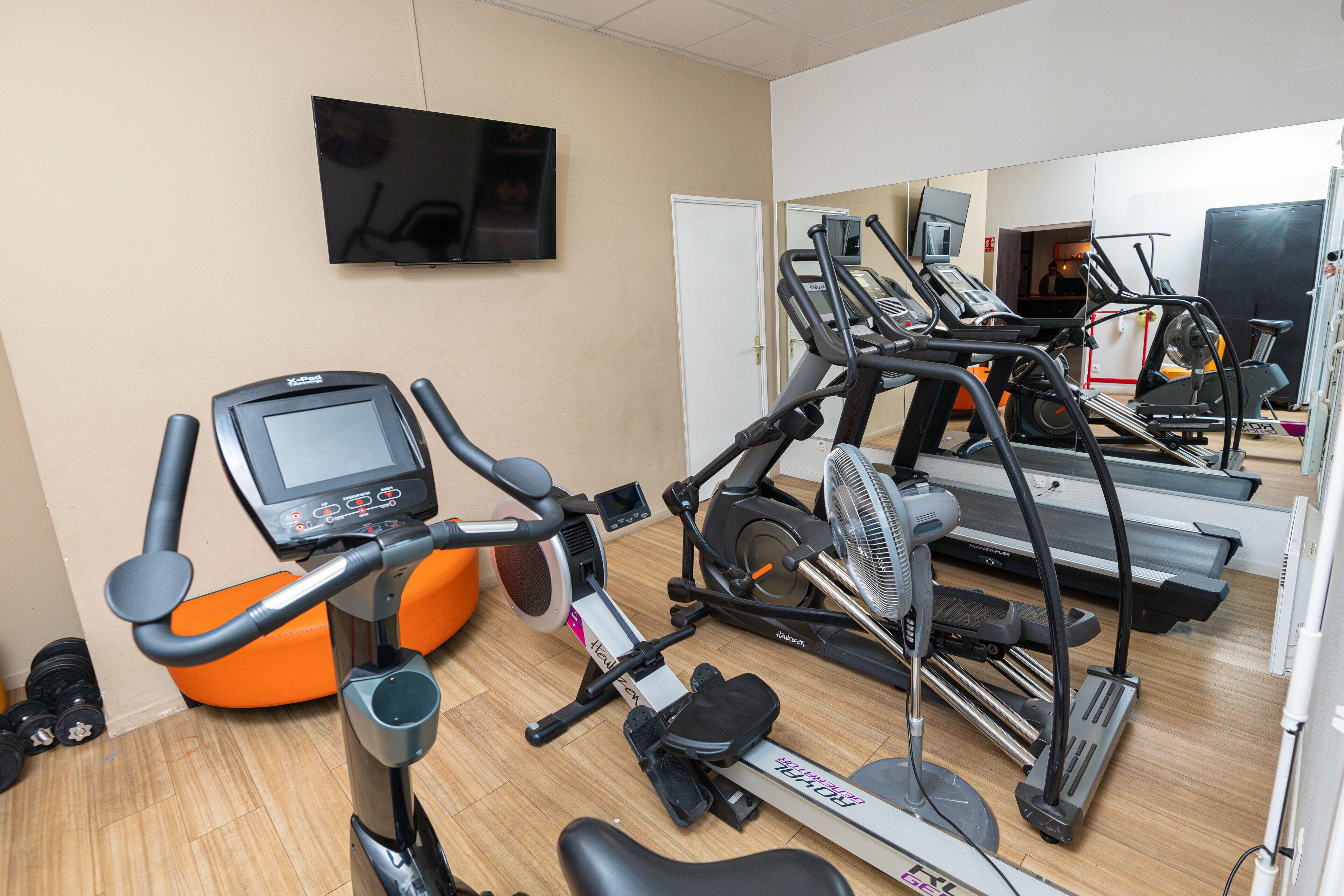 Un gimnasio con equipo de ejercicio, incluyendo cintas de correr y una máquina elíptica, y un televisor montado en la pared.
