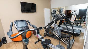 Un gimnasio con equipo de ejercicio, incluyendo cintas de correr y una máquina elíptica, y un televisor montado en la pared.