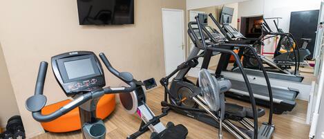 Un gimnasio con equipo de ejercicio, incluyendo cintas de correr y una máquina elíptica, y un televisor montado en la pared.