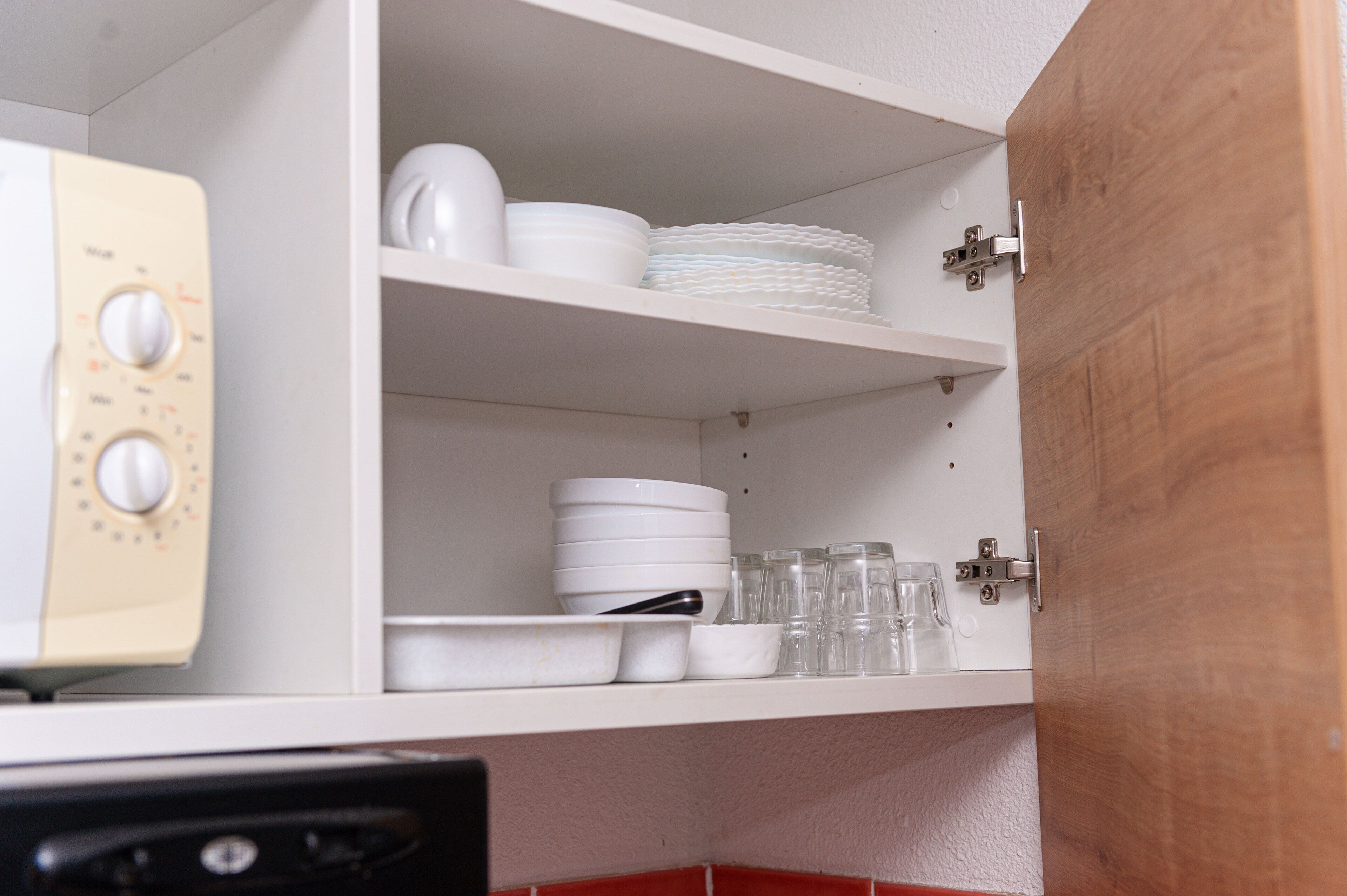 A kitchen with white shelves holding dishes, glasses, and a microwave.
