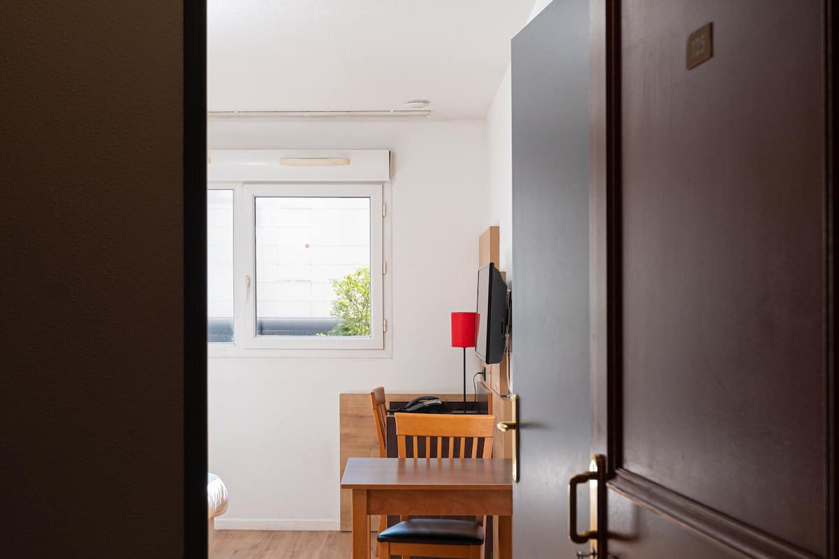 An open door leading to a dining area with a wooden table and chairs, a television, and a window with natural light.