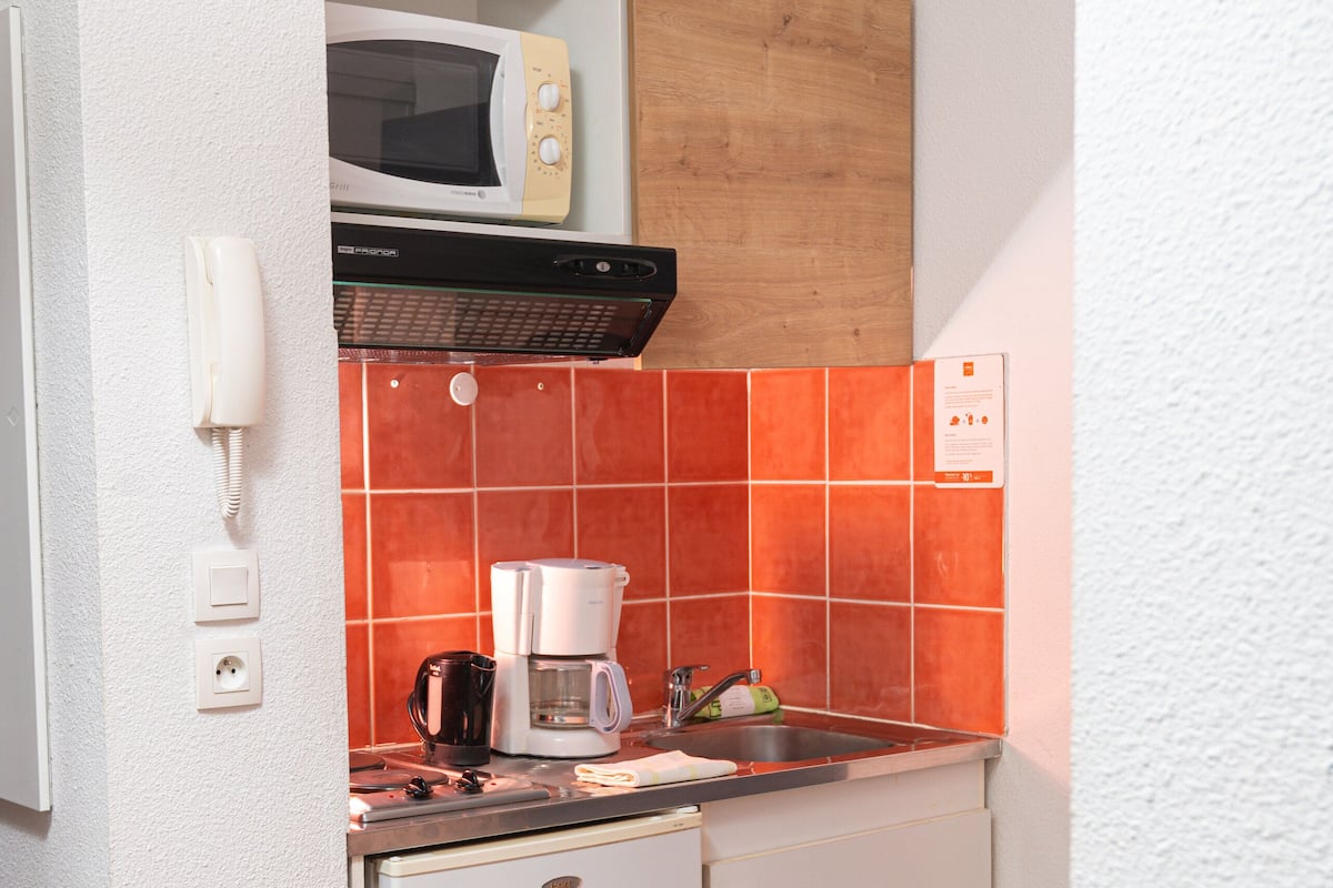 A compact kitchenette with a microwave, coffee maker, and sink.
