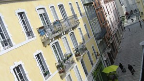 Een meerlaags gebouw met balkons, een café met terras en een geplaveid straatje.