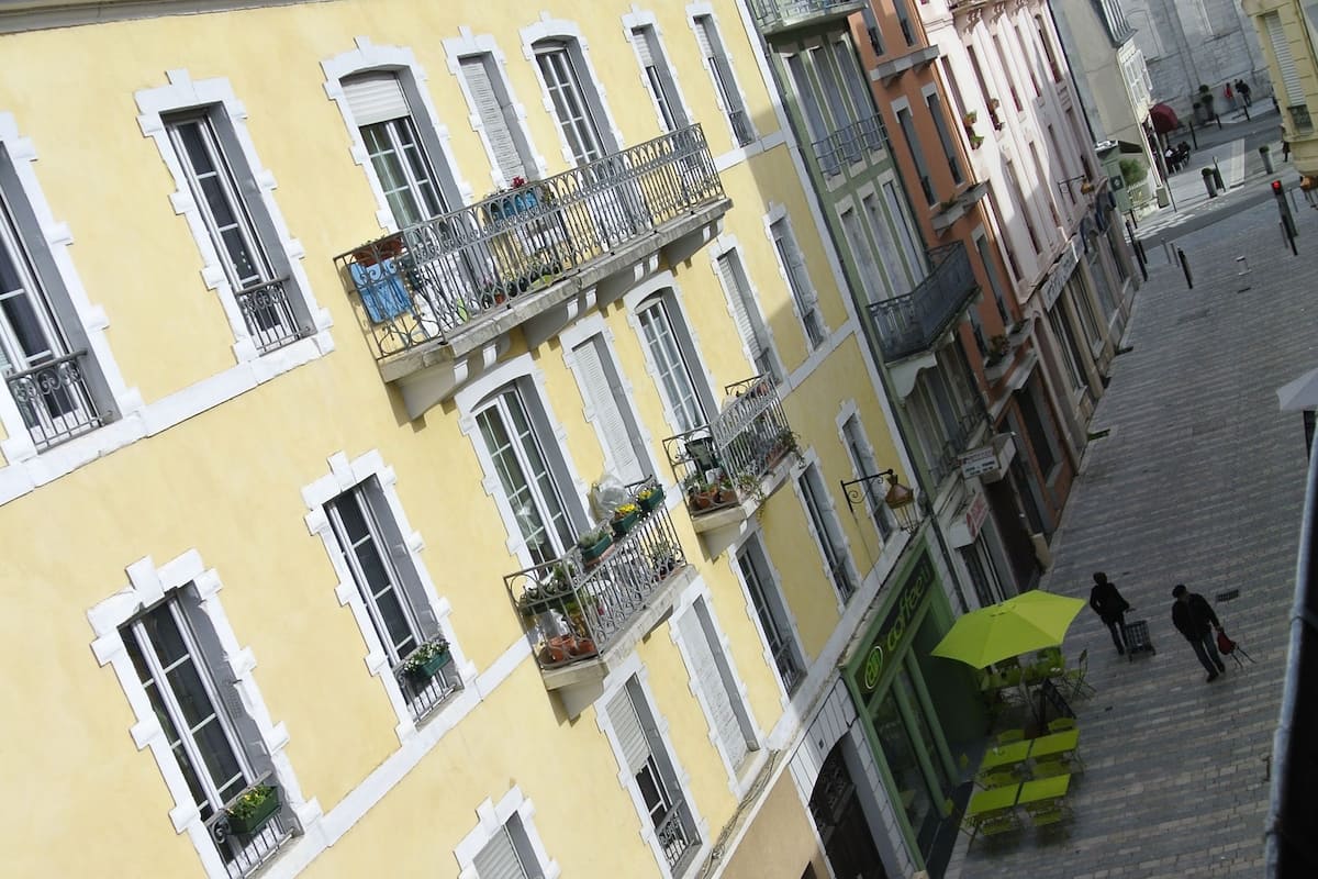 Un immeuble à plusieurs étages doté de balcons, un café avec une terrasse, et une rue pavée.