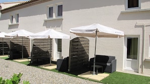 A row of outdoor seating areas with umbrellas, a building with a tiled roof, and a door. - Brit Hotel Bosquet (Carcassonne)
