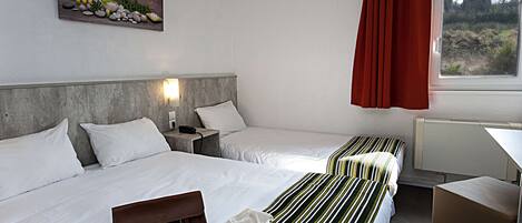 A hotel room with two beds, a wooden headboard, a painting on the wall, a window with red curtains, and a bedside lamp.