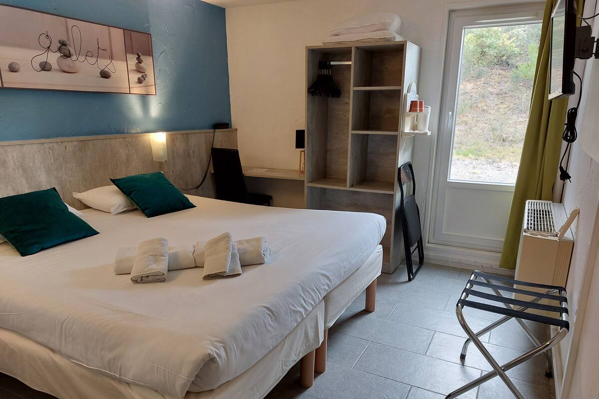 Une chambre d’hôtel avec un lit, des oreillers, un porte-serviettes, une étagère avec des articles de toilette et une vue sur l’extérieur.