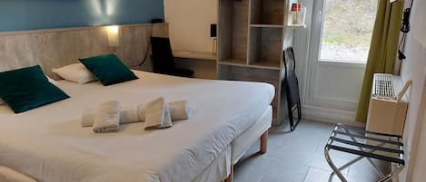 A hotel room with a bed, pillows, a towel rack, a shelf with toiletries, and a view of the outdoors.