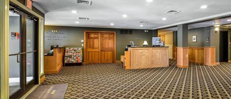 A reception area with a patterned carpet, wooden reception desk, and a guest services sign.