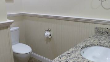 A bathroom with a toilet, a sink, and a marble countertop.