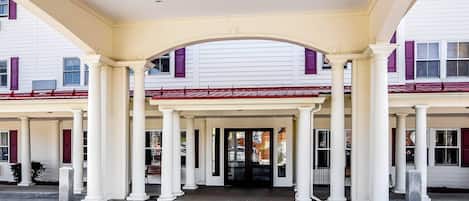 A building entrance with a covered porch supported by columns, leading to a door with glass panels.