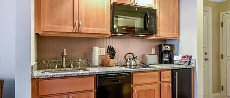 A compact kitchen with wooden cabinets, a stainless steel microwave, a dishwasher, and a granite countertop.