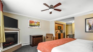 A hotel room with a bed, a fireplace, a ceiling fan, a chair, a kitchen area, and artwork on the walls. - Bluegreen Vacations South Mountain, an Ascend Collection Resort (Lincoln)