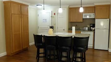 A kitchen with wooden cabinets, a white refrigerator, a microwave, and a dining area with four chairs.