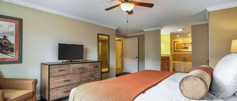 A hotel room with a bed, a television on a wooden dresser, a ceiling fan, and a door leading to a bathroom.