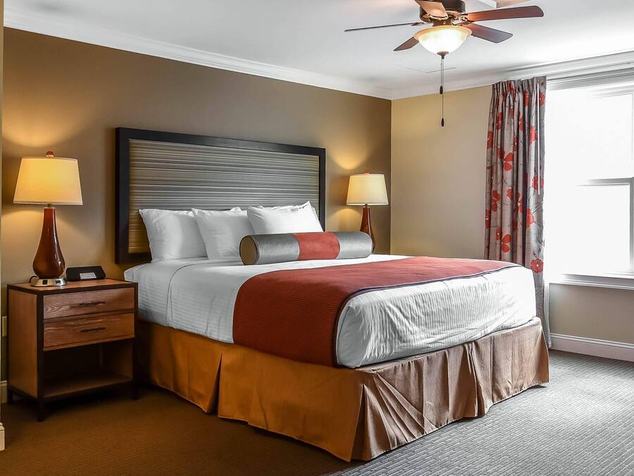 Ein Hotelzimmer mit einem großen Bett, zwei Nachttischlampen, einem Nachttisch, einem Deckenventilator und einem Fenster mit Vorhängen.