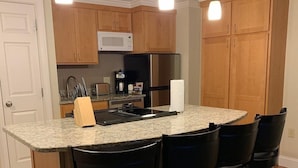 A kitchen with wooden cabinets, a microwave, a refrigerator, a granite countertop, and four black bar stools. - Bluegreen Vacations South Mountain, an Ascend Collection Resort (Lincoln)