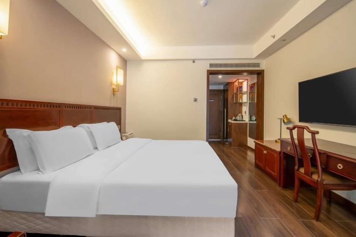 A hotel room with a large bed, a TV, a desk, and a chair.